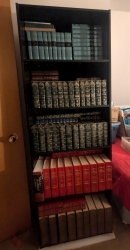 A black bookshelf with Bible commentaries and study books stacked and doubled up.